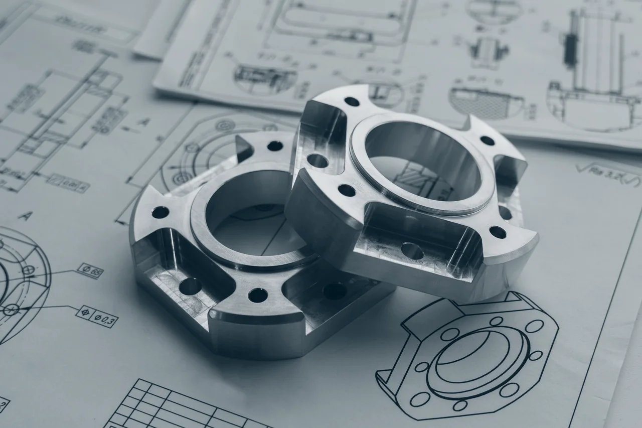 Zwei gefräste Präzisionsteile aus Metall auf technischen Zeichnungen